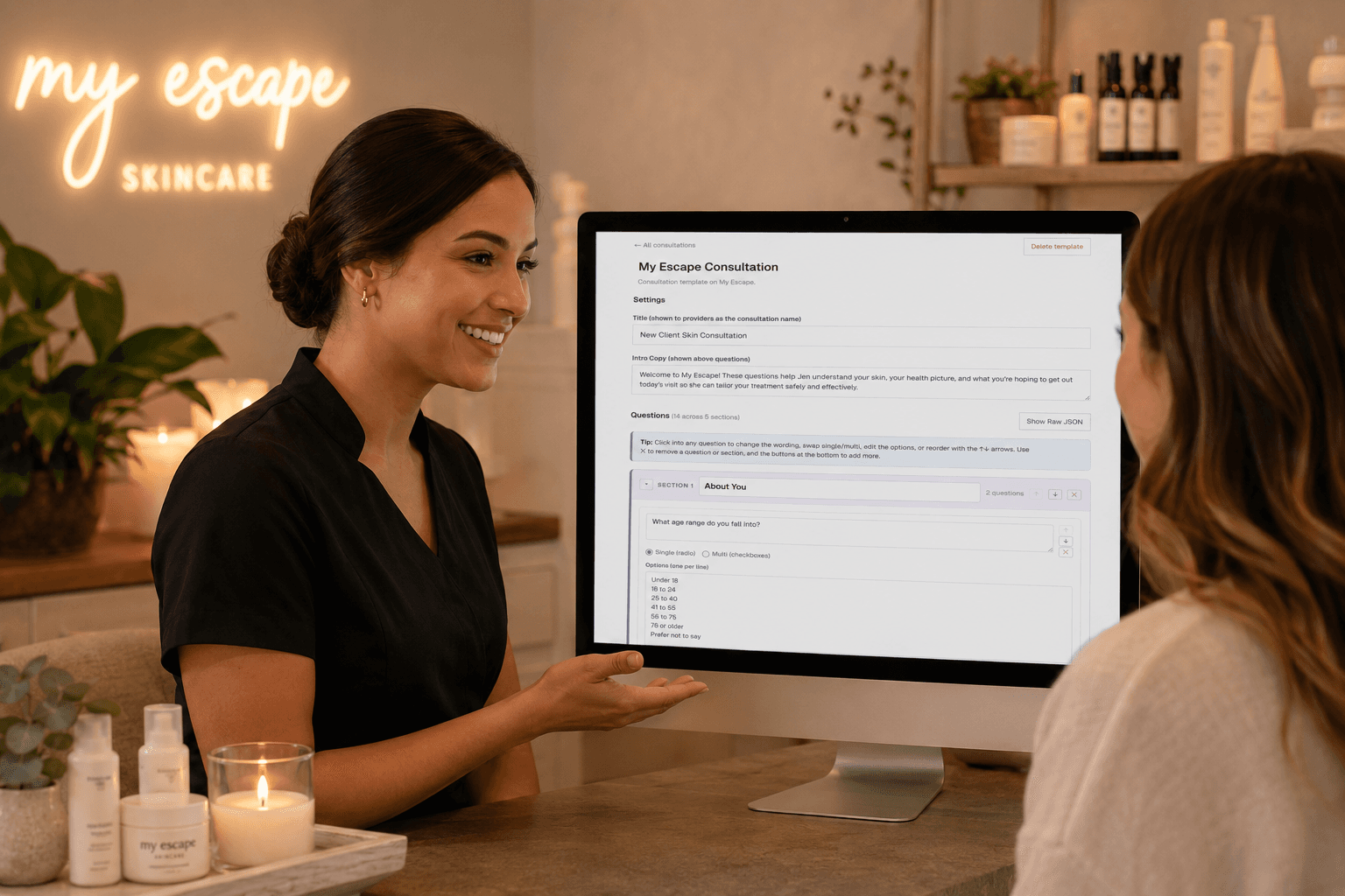 A spa practitioner walking a client through a consultation template on a desktop monitor inside a warmly lit My Escape Skincare consultation room